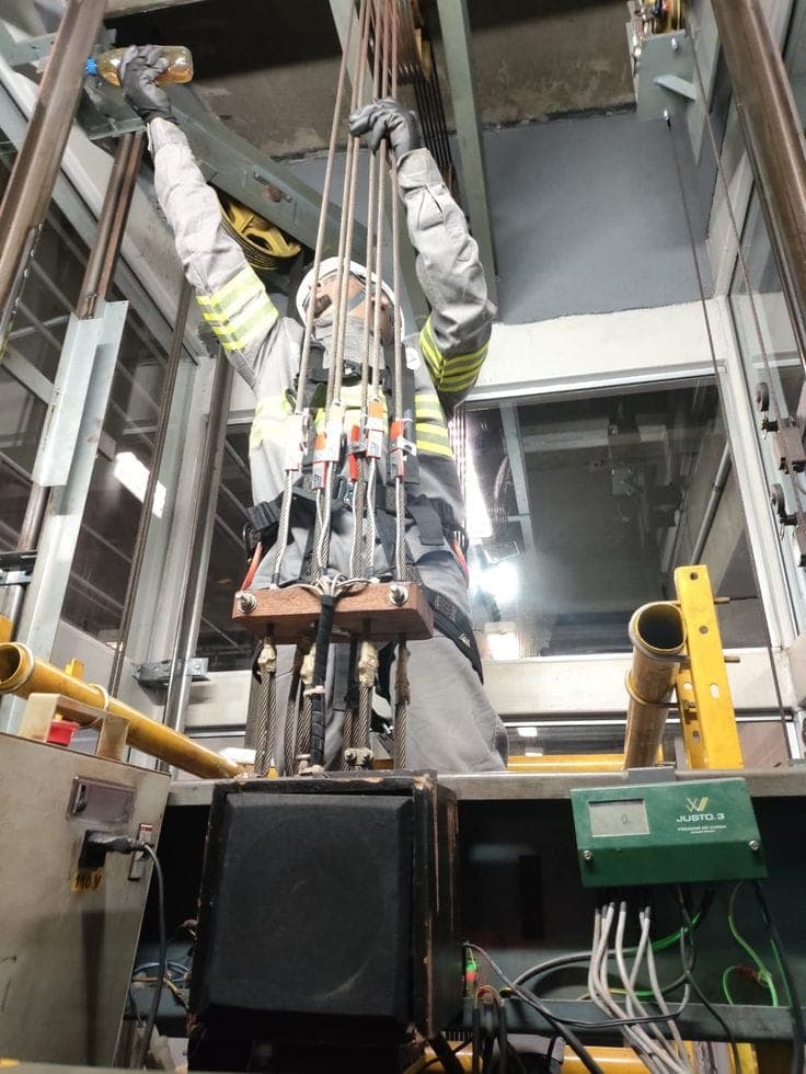 Elevator technician inspecting and working on the lifting cables and machinery inside an elevator shaft.